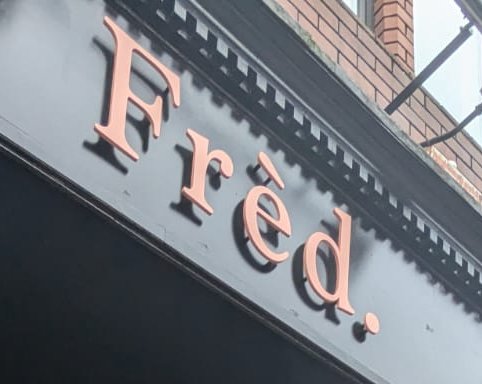 The 'Frèd.' wordmark in coral on the shopfront's black fascia.